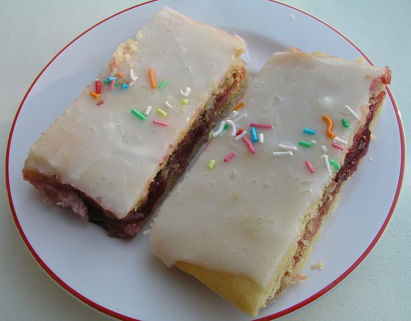 Dos hindbærsnitter con glaseado blanco y virutas de colores en un plato