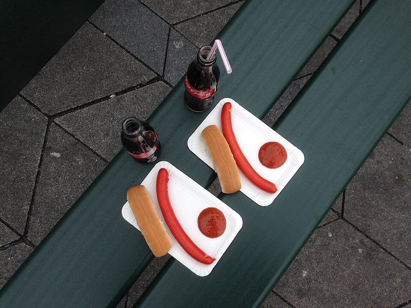 Dos platos de røde pølser con pan y kétchup en un banco de la calle