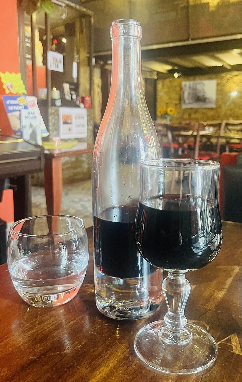 Un pot lyonnais de vino tinto junto a una copa